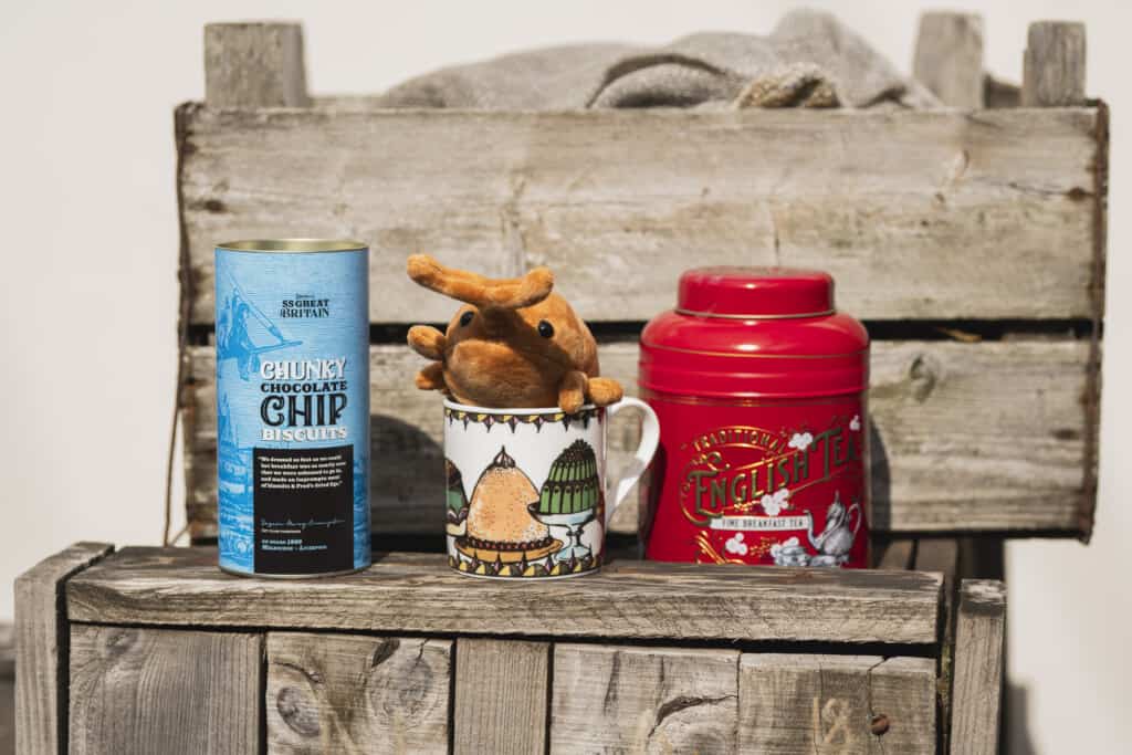 Outside on a storage crate. A blue tin of milk chocolate biscuits, pudding mug, Winnie the Weevil soft toy and English Breakfast Tea Caddy for Instagram/Facebook Giveaway. 