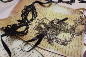 A black and a gold lace mask lying on a old piece of beautifully handwritten paper.